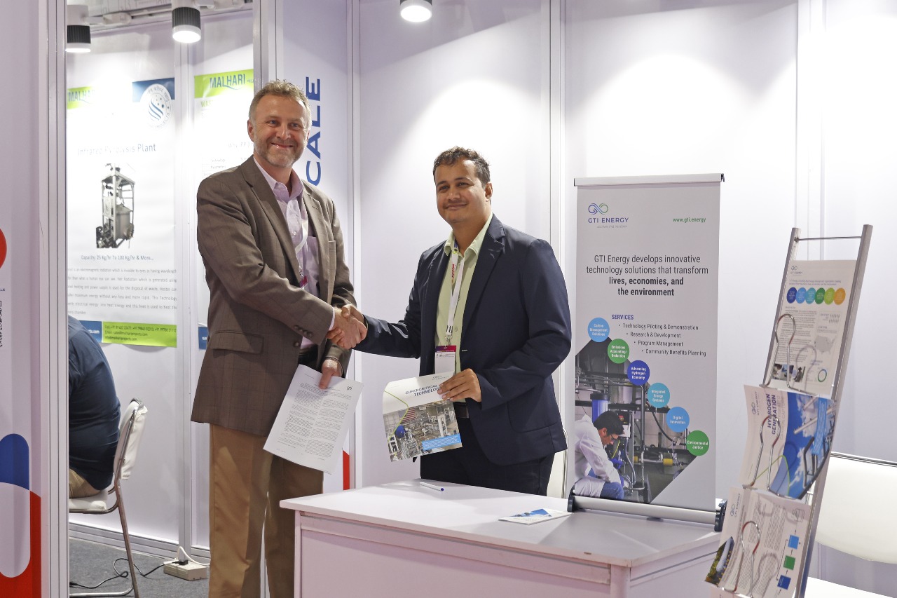 Two exhibitors shake hands at a stand, papers in hand.