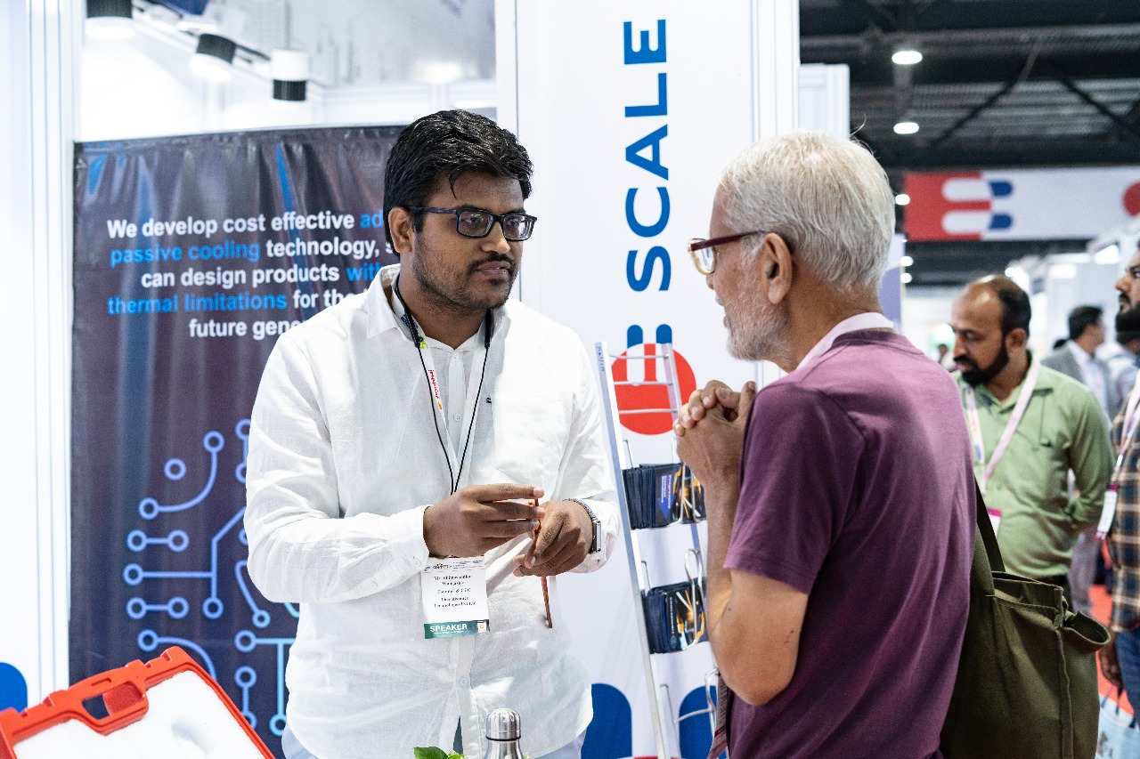 A speaker explains a cooling technology to a visitor beside a SCALE banner.