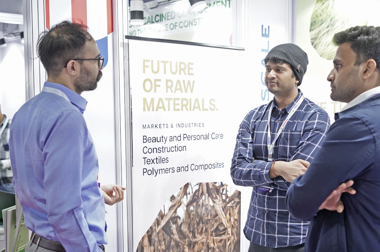 Three people in conversation at a raw materials stand.